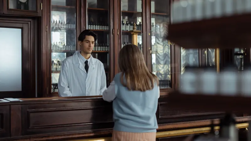Una mujer de espaldas frente al mostrador de una farmacia, esperando a que la atiendan.